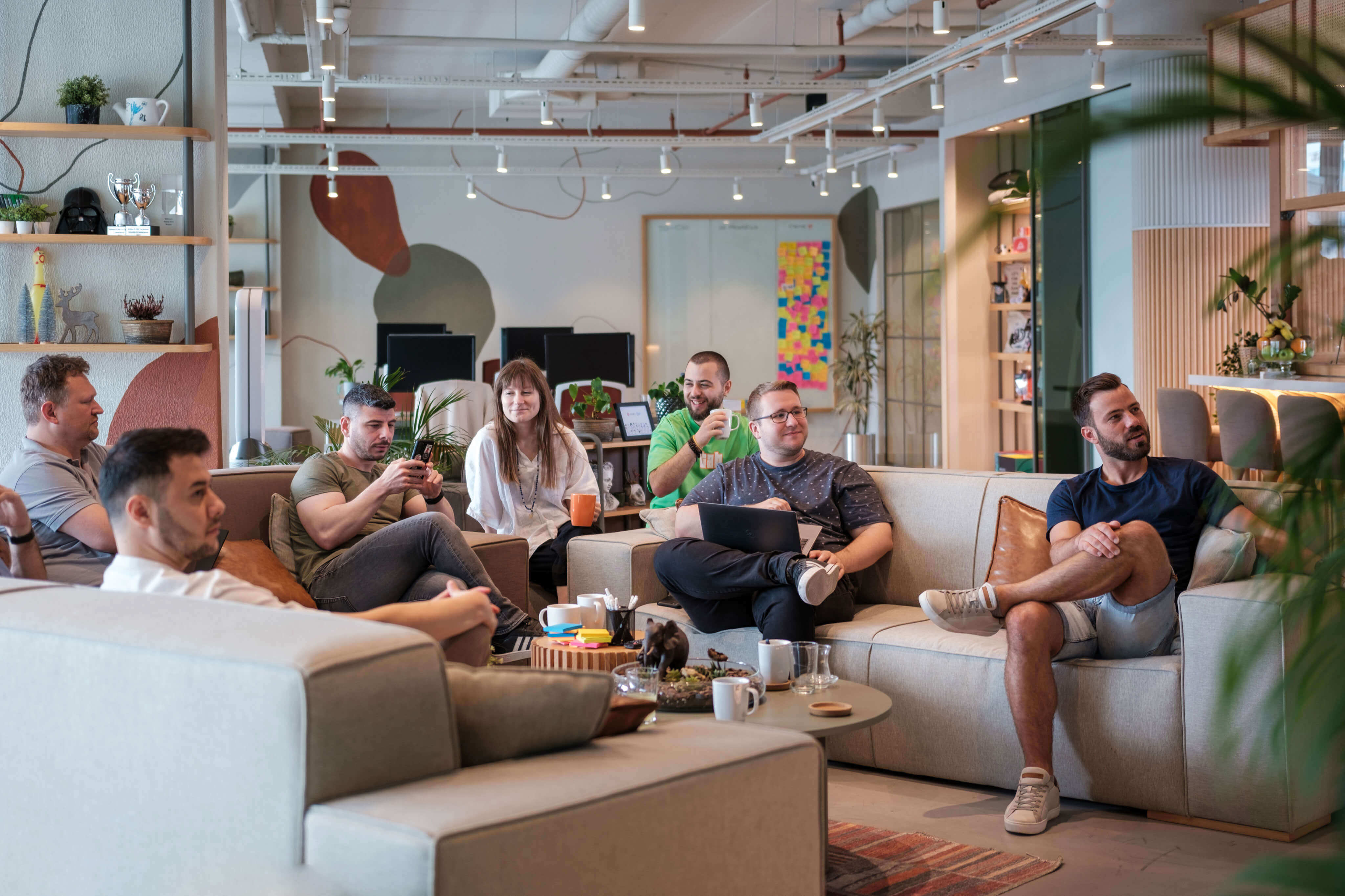 A diverse group of people gathered on spacious grey couches in an office, smiling, and facing a direction.