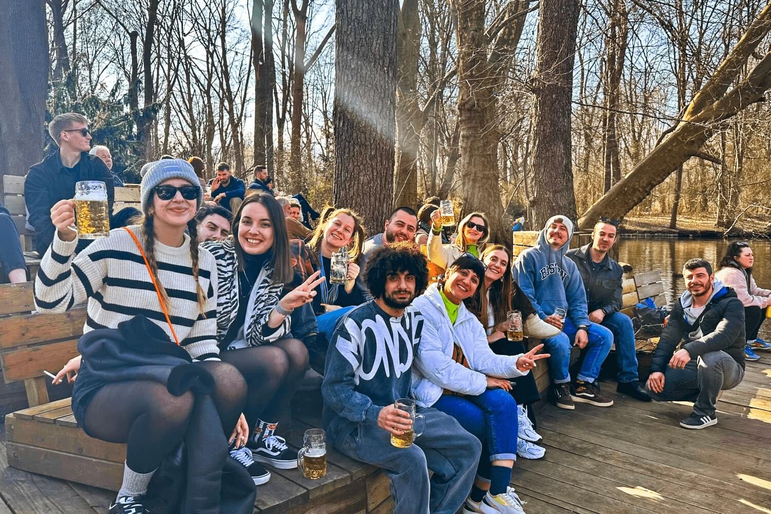A group of Atolye15 employees in the woods, sitting by a lake and raising beer glasses in a Biergarten in Berlin.