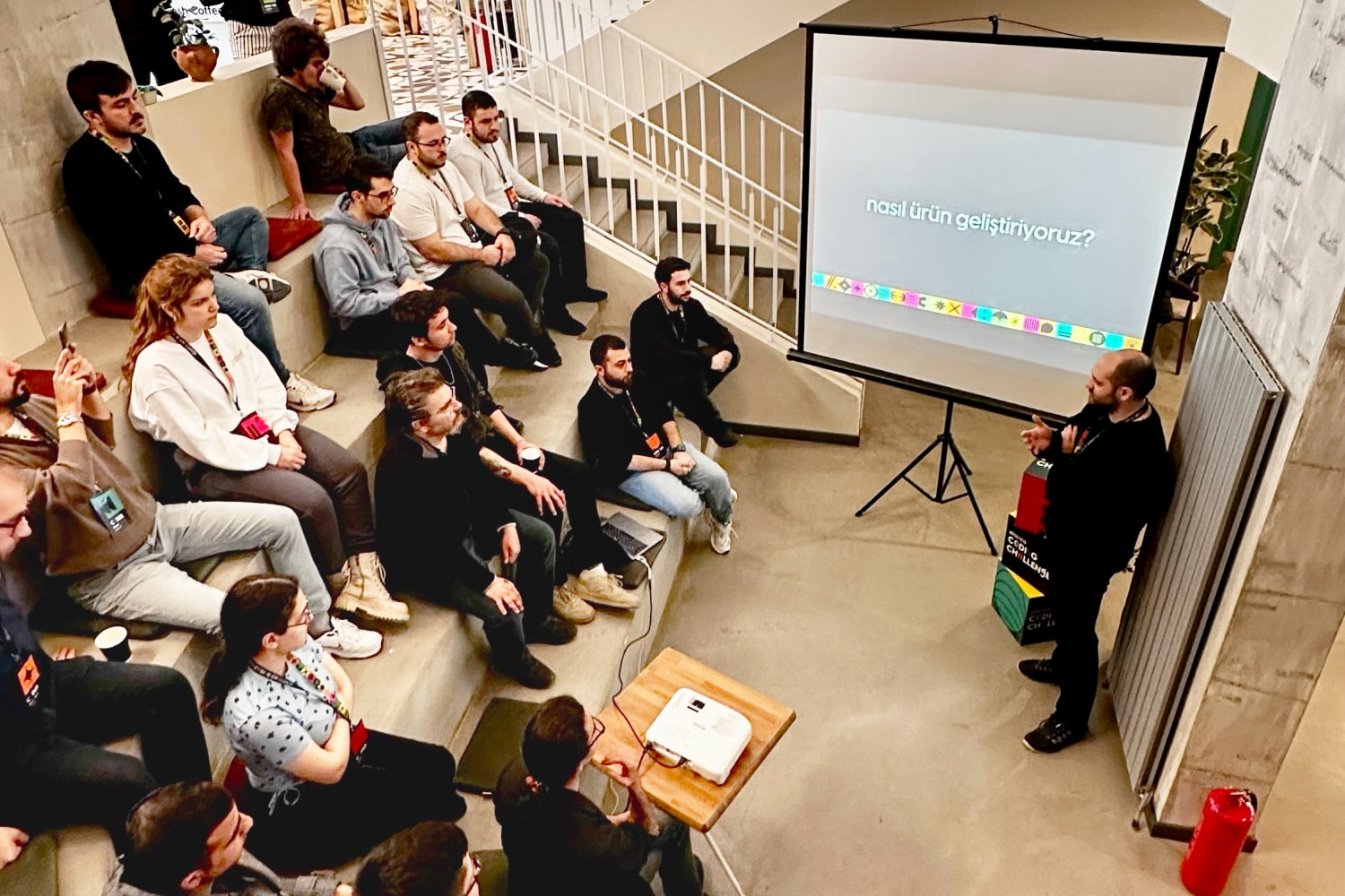 Coding Challenge Ankara participants sitting at a lecture hall listening to the lead frontend developer Erinç Fırtına about how Atolye15 develops products.