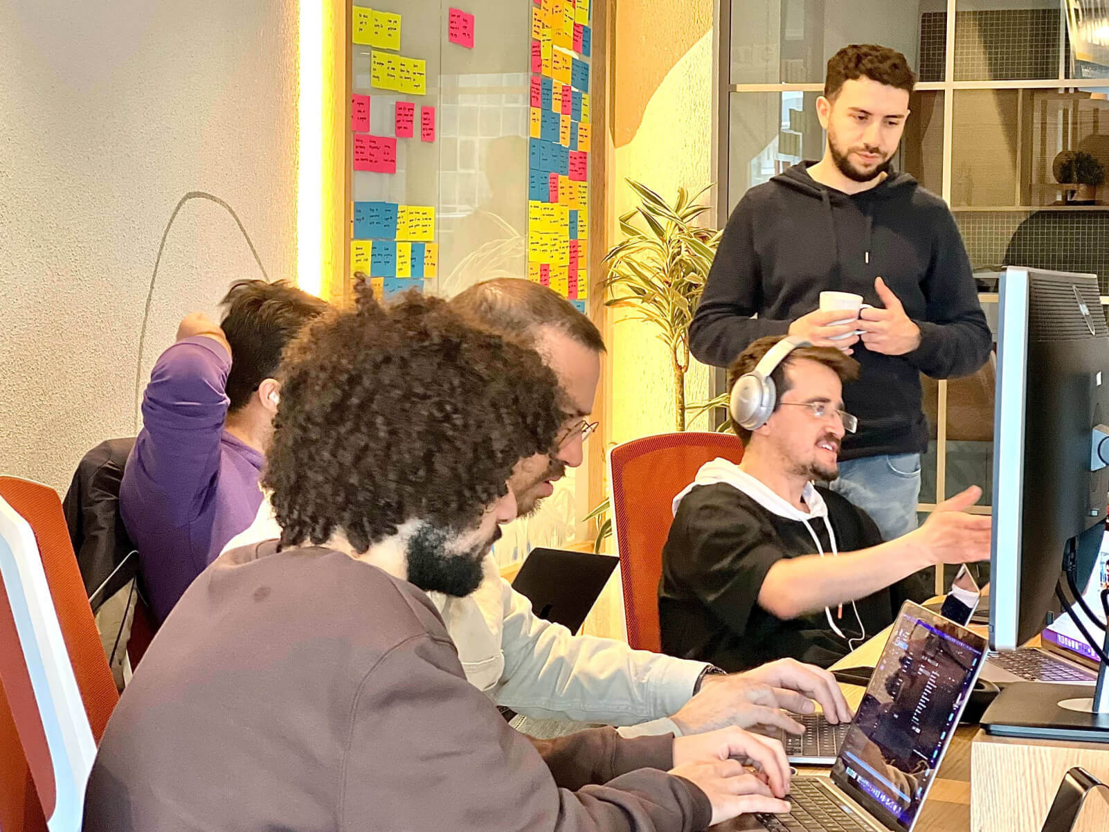 Employees of Atolye15 working at their computers and engaging in discussions in the office with a task board visible in the background.