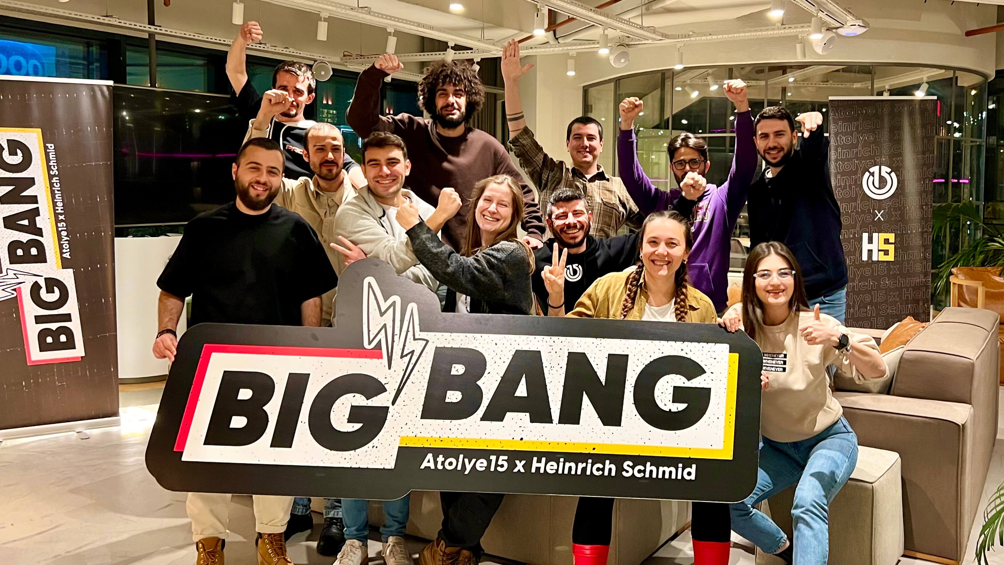 A proud and smiling group of people gathered behind the 'Big Bang' sign with Atolye15 and Heinrich Schmid written underneath.