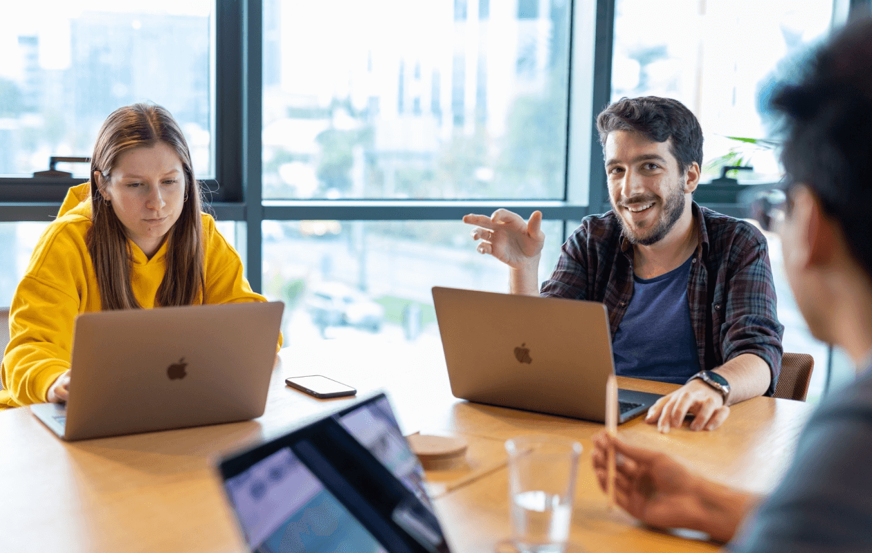 Two focused coworkers with laptops in a meeting, with a man explaining something and a woman listening intently.