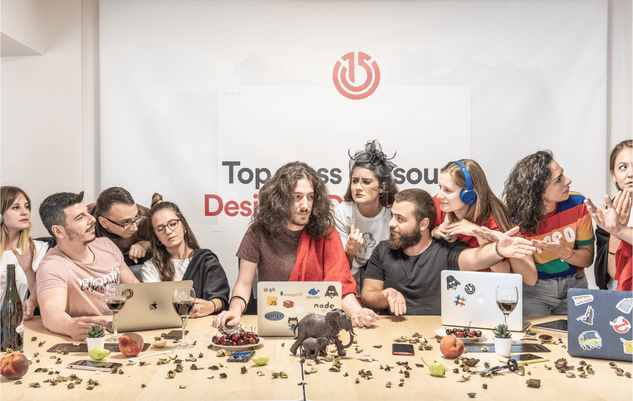 Creative team reenacting the last supper around a table with laptops and decorations, Atolye15 logo in the background.