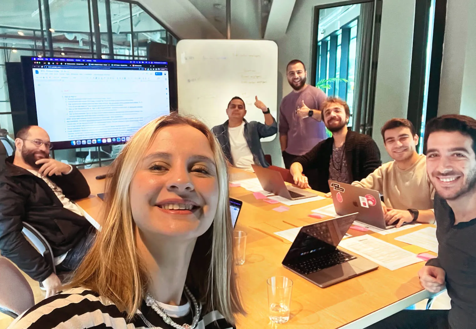 Team meeting with one member taking a selfie and others posing happily in the background.