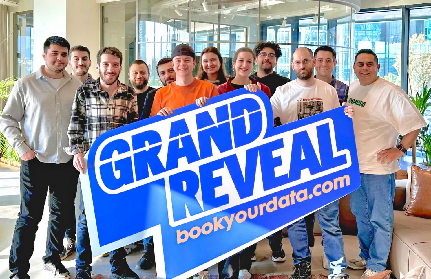 Group of Atolye15 team members holding a 'GRAND REVEAL' sign for bookyourdata.com.