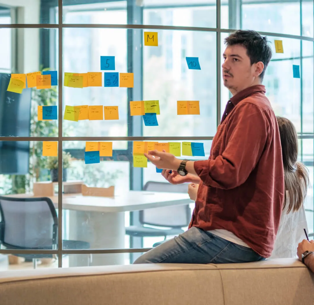Man planning with sticky notes on a glass wall in an office.