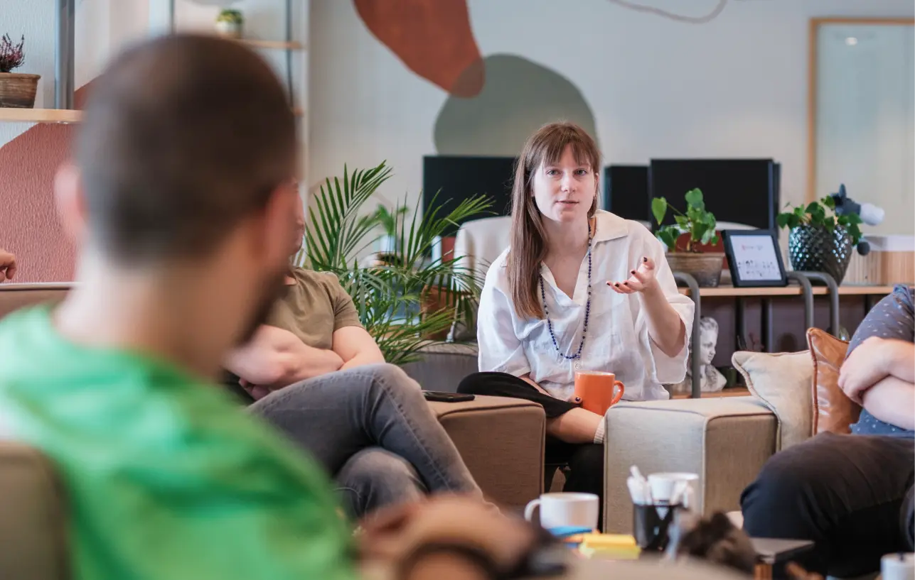 Team member shares ideas during a relaxed team conversation in a cozy, plant-filled workspace.