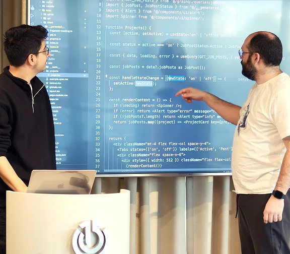 Two developers discussing the project on a laptop, with one person leaning in to guide the other.