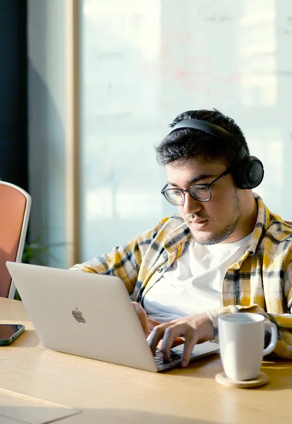 Developer with a beanie and glasses working carefully on a laptop at a well-lit desk.