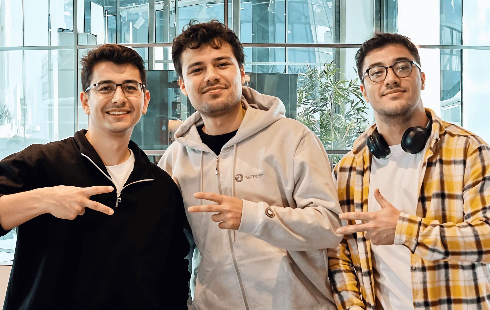 Three developers posing together, smiling and flashing peace signs in a bright office.