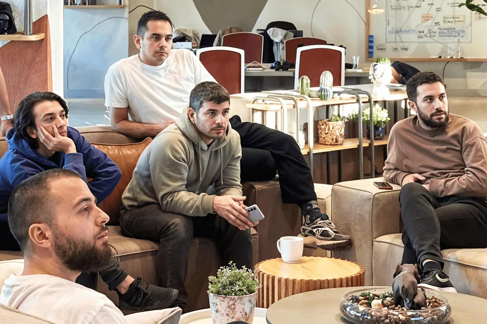 Team members sitting on a couch, attentively watching a presentation in a relaxed office setting.