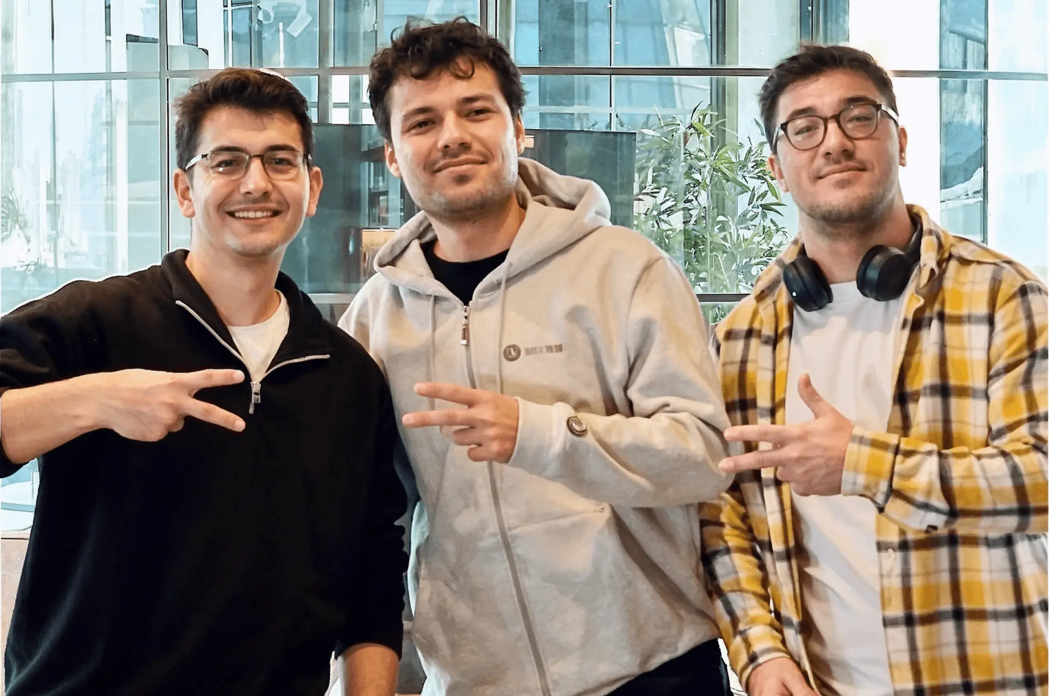 Three smiling developers posing for a photo, flashing peace signs in a modern office.
