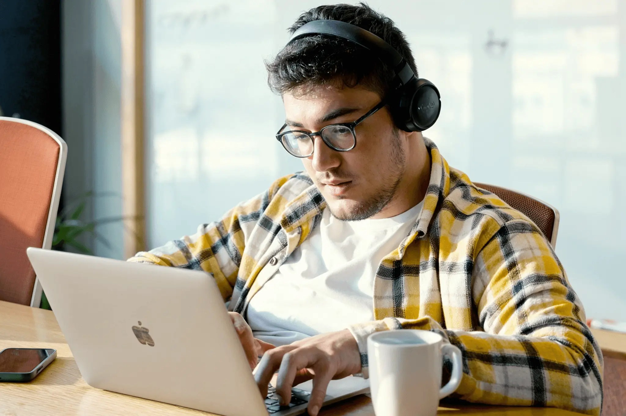 Developer wearing headphones, focused on typing at a laptop with a mug beside him.