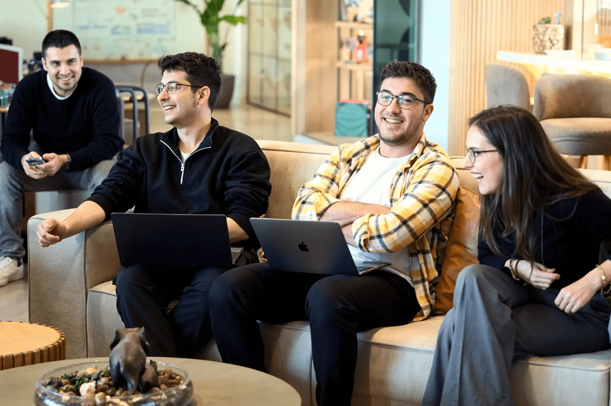 Group of developers laughing and chatting with laptops in a cozy office lounge.